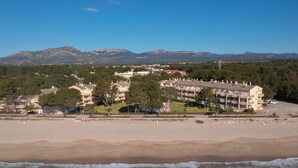 Ein Hotel an der Küste mit mehreren Etagen, ein Strand im Vordergrund und Berge im Hintergrund.