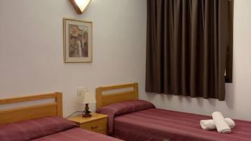 Ein Hotelzimmer mit zwei Betten, einem Nachttisch mit Lampe, einem gerahmten Bild an der Wand und einem Fenster mit Vorhängen.