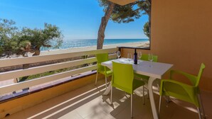 En balkon med et bord og stole, med udsigt over en strand.