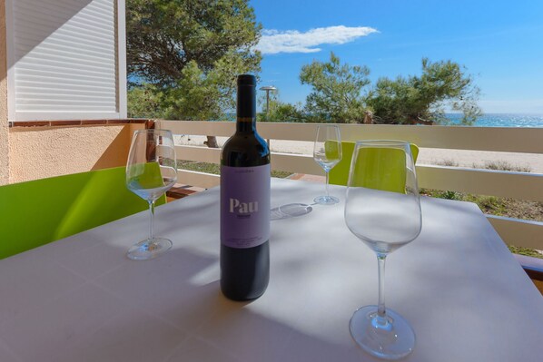 A table with a bottle of Pau wine and two wine glasses, set against a scenic view of the sea and trees.