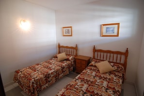 A bedroom with two single beds, a nightstand, and a wall-mounted light.