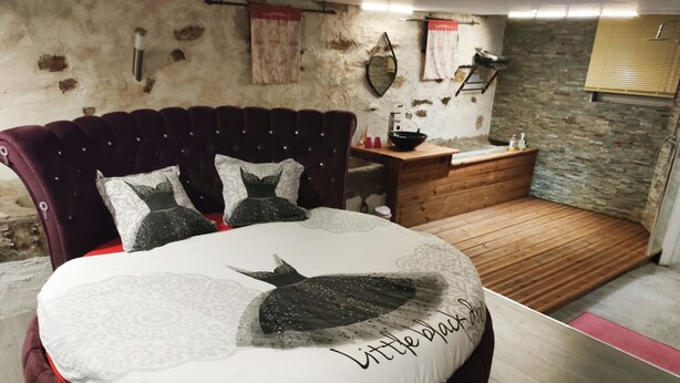 Uma cama redonda com edredom branco e cinza e almofada decorativa preta.
