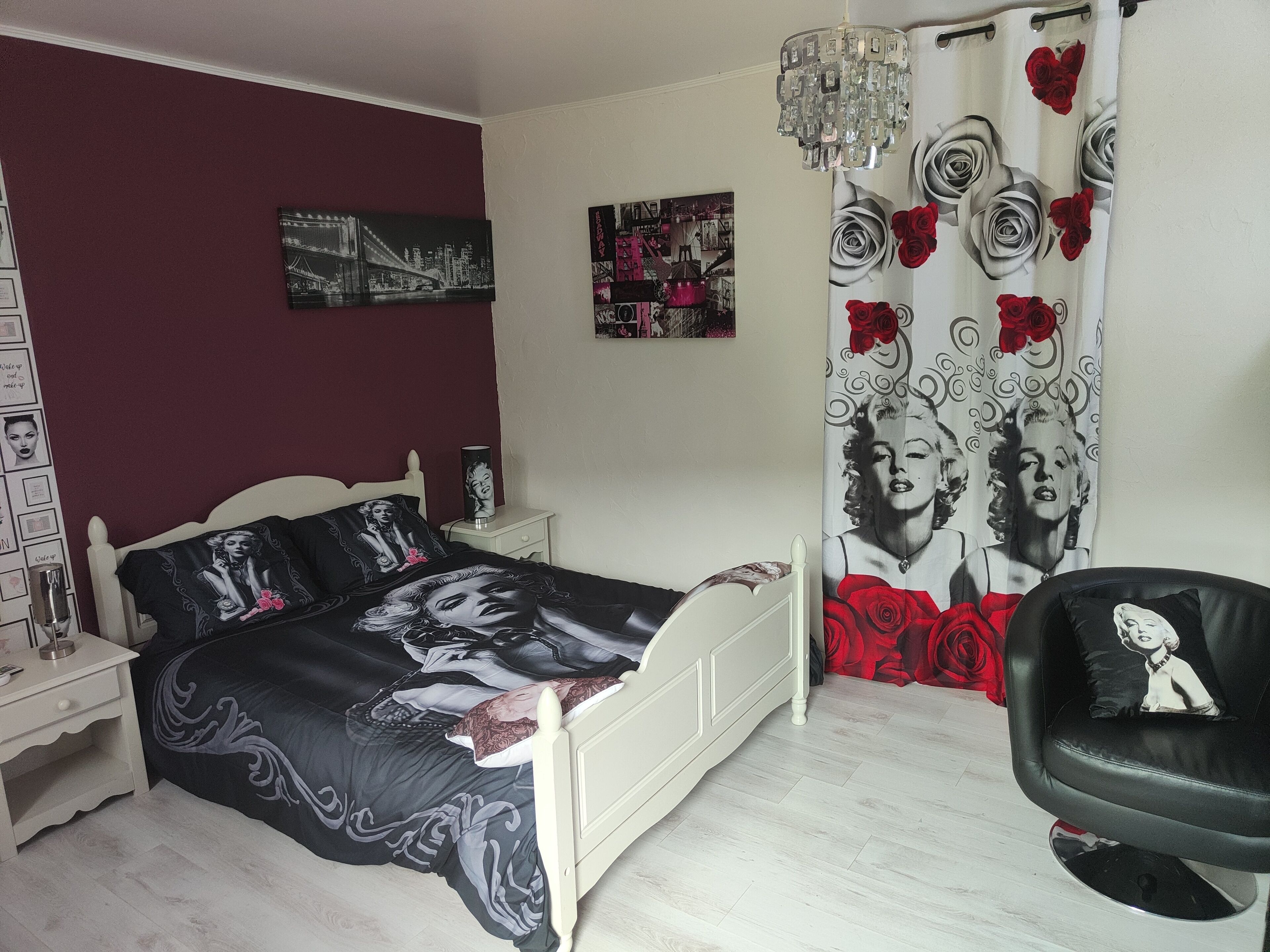 Quarto com cama, mesa de cabeceira, cadeira, lustre e cortina estampada com rosas.