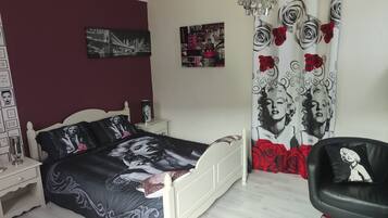 Quarto com cama, mesa de cabeceira, cadeira, lustre e cortina estampada com rosas.
