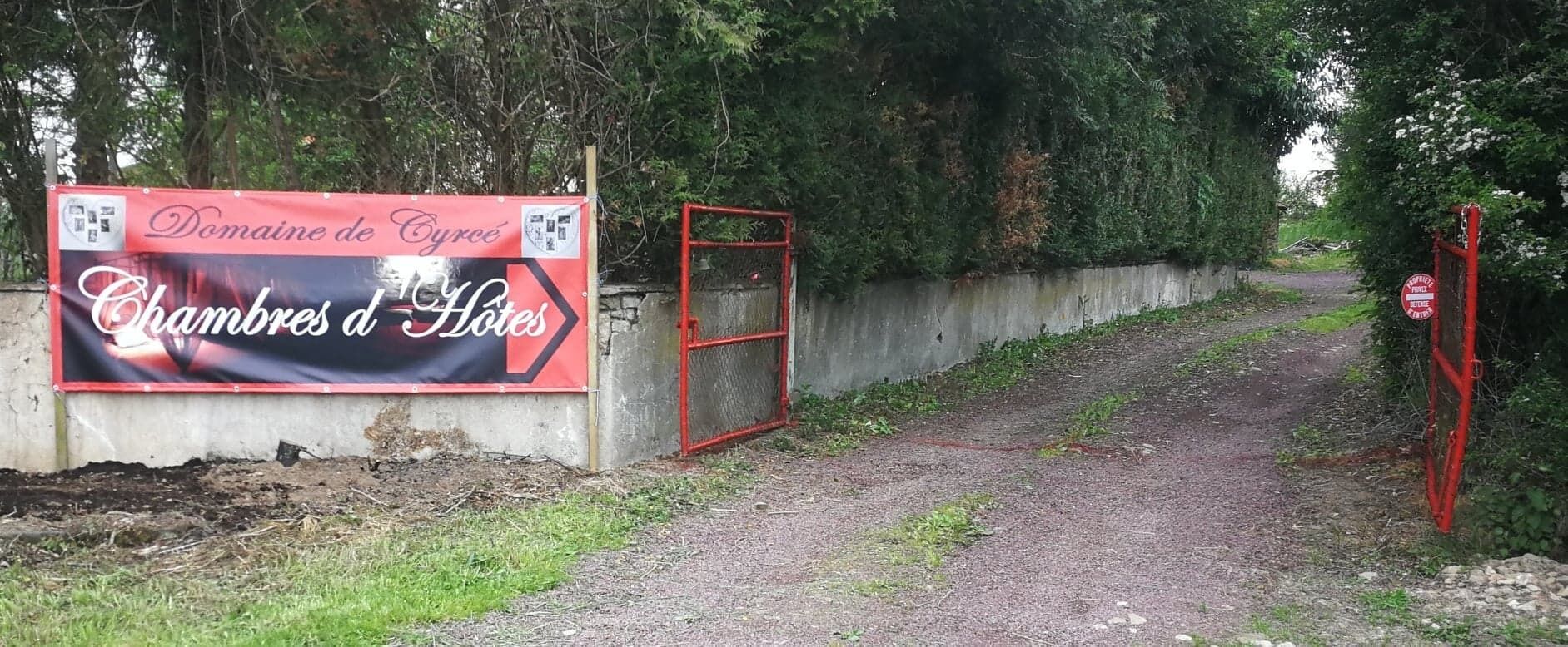 A sign for Domaine de Cyrée Chambres d'Hôtes with a red gate and a dirt path.