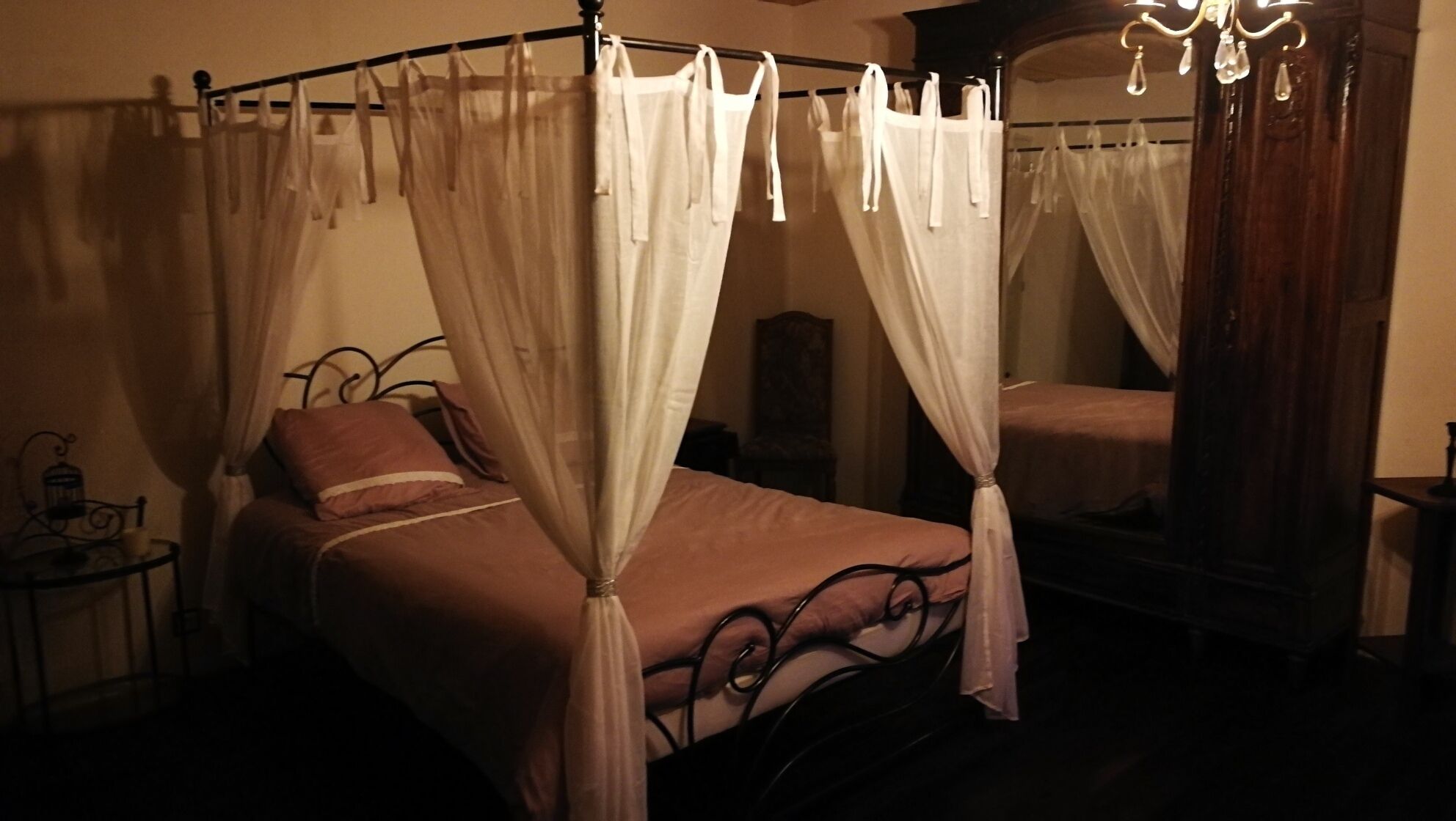 A four-poster canopy bed with a mirror and a chandelier.