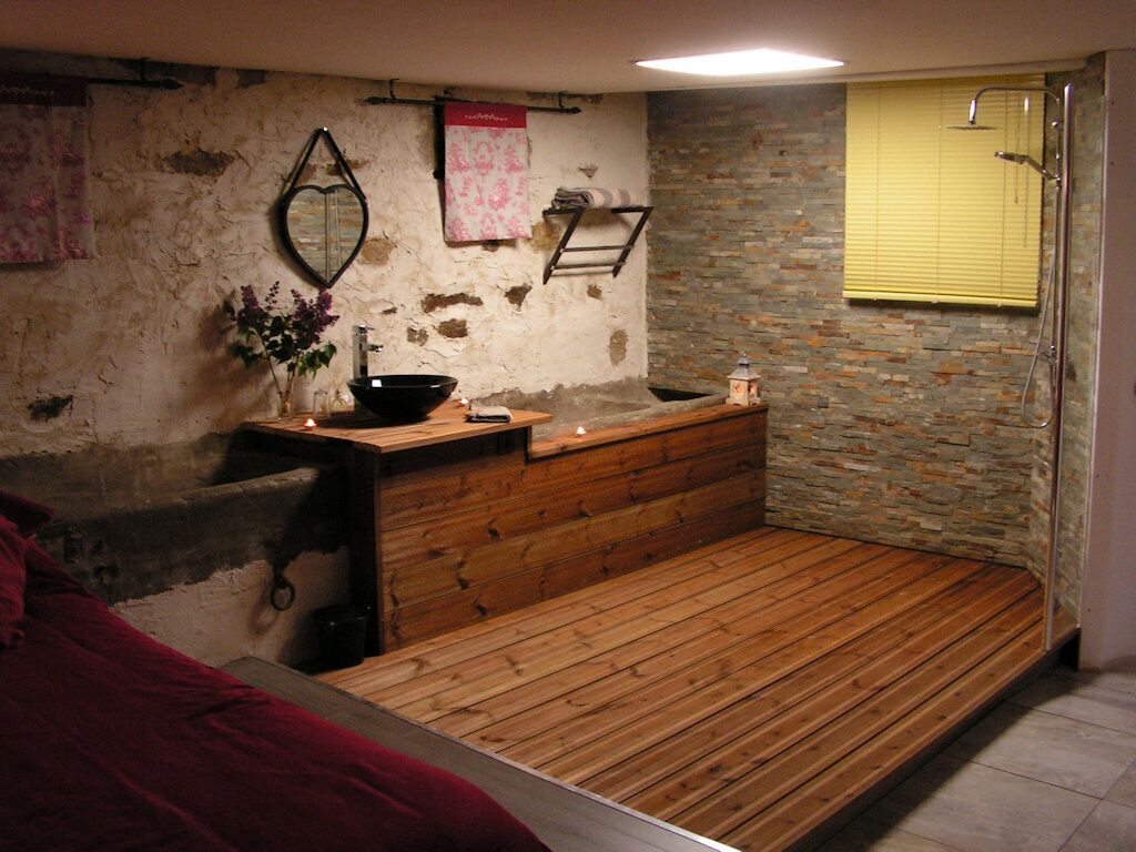 A small, rustic bathroom with a wooden bench, a stone wall, and a shower area.