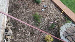 Uma área de pátio com deck de madeira, móveis de exterior e um pequeno jardim com cobertura de cascalho e plantas.