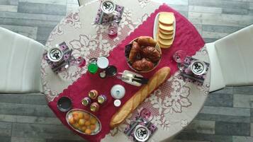 Una mesa dispuesta con comida y bebidas, incluyendo pan, pasteles y una taza de café, sobre un mantel estampado.