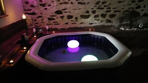 Uma banheira de hidromassagem com duas esferas iluminadas, uma parede de pedra e uma pequena planta no canto.