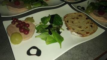 Un plato con una rebanada de pan, uvas, una ensalada de hojas y un trozo de carne.