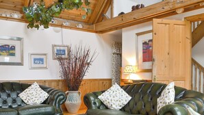 A cozy living room with two green leather sofas, a vase with branches, and wooden paneling on the walls. - 1 bedroom accommodation in Fearnmore, near Applecross (Fearnmore, near Applecross)