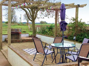 Um alpendre externo com pérgola, mesa de vidro e cadeiras.