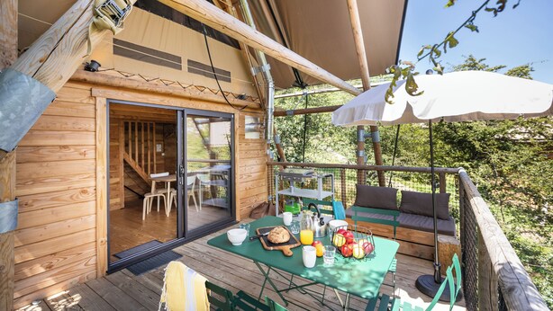 Una cabaña de madera con terraza, mobiliario exterior y una mesa para el desayuno.