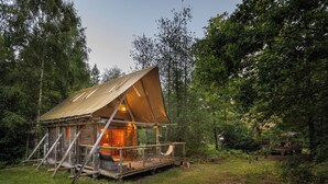 Una cabaña de madera rústica con techo inclinado, rodeada de un bosque denso.