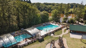 Una piscina exterior con zona techada, rodeada de árboles y vista al río.