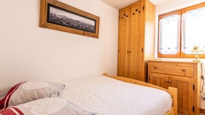 A bedroom with a bed, a wooden wardrobe, a dresser, a framed picture on the wall, and a window with curtains. - Lovely apartment at the bottom of the slopes (MORZINE)
