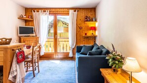 A cozy room with a wooden desk, a TV, a sofa, and a balcony with a wooden railing. - Lovely apartment at the bottom of the slopes (MORZINE)