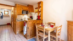 A kitchen with wooden cabinets, a dining table with chairs, and a red kettle. - Lovely apartment at the bottom of the slopes (MORZINE)