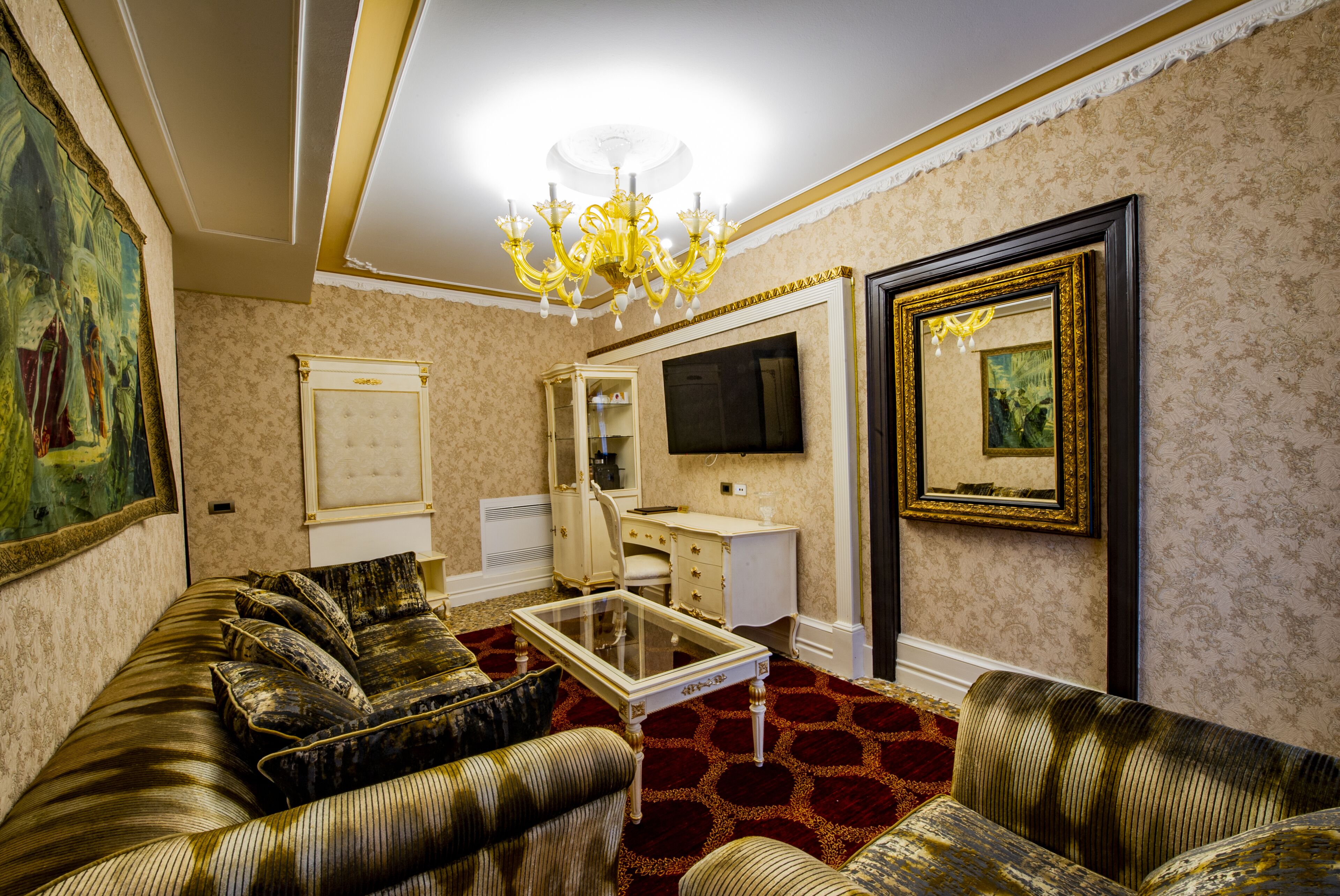 A living room with a sofa, armchairs, a coffee table, a TV, a cabinet, and a chandelier.