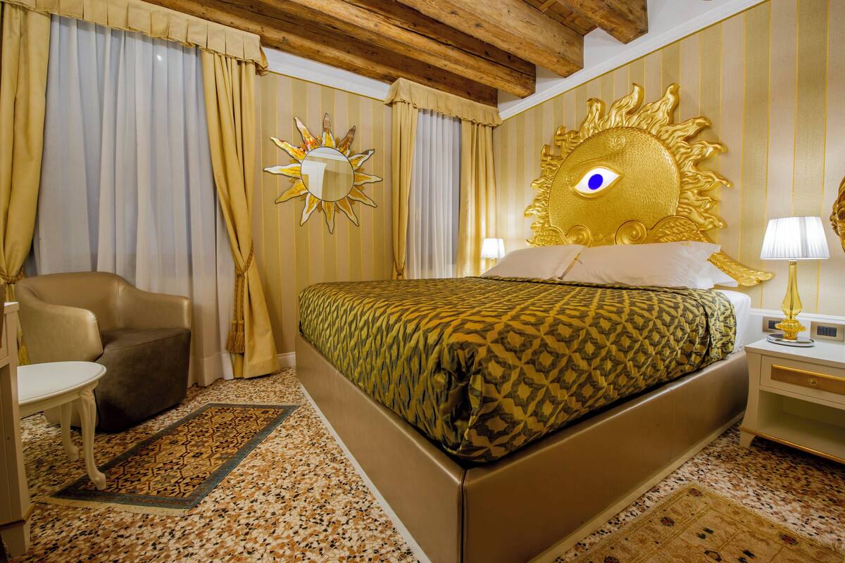 A hotel room with a large bed, a chair, a nightstand, and a sun-shaped wall decoration.