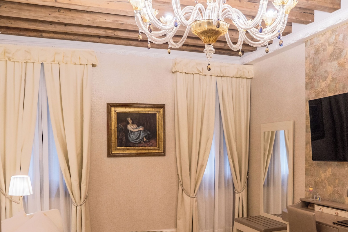Een hotelkamer met een rond bed, een bureau, een stoel, een kroonluchter en een schilderij aan de muur.