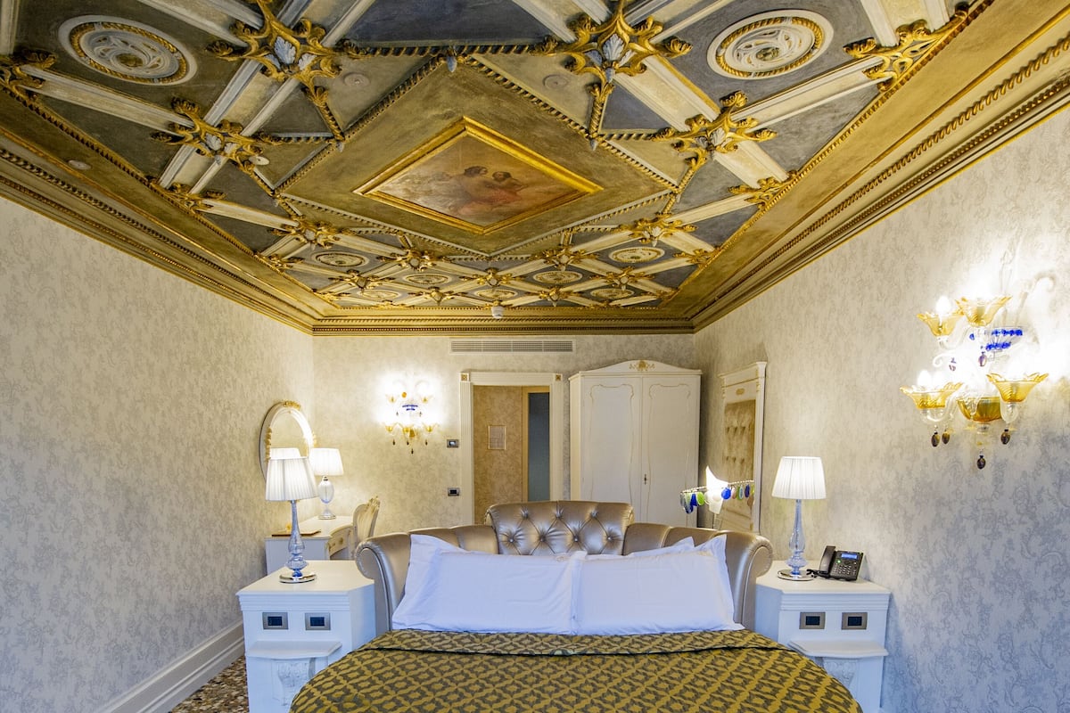 A luxurious bedroom with a large bed, ornate ceiling, and classic decor.