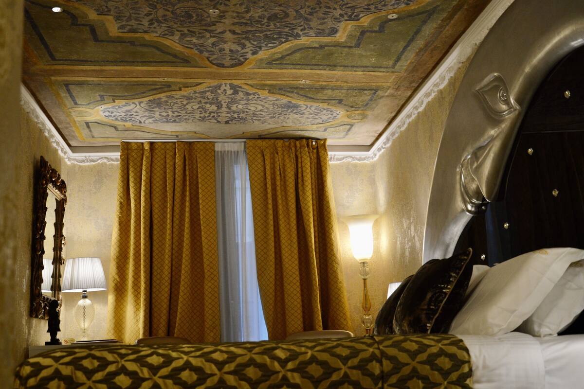 A hotel room with a patterned bedspread, a large mirror, and a decorative ceiling.