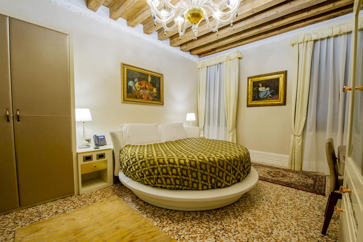 A hotel room with a bed, a desk, a chair, a wardrobe, and two paintings on the walls.