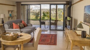 Un salon comprenant un canapé, des fauteuils, une table et une vue sur l’extérieur, visible à travers une porte vitrée.