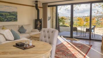 Una sala de estar con una mesa redonda de madera, un sofá y vistas a un patio exterior a través de un ventanal.