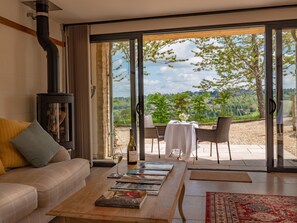 A cozy living room with a sofa, a coffee table with books, a wine bottle, and a fireplace. - Woodchester Valley Vineyard Barns (Stroud)