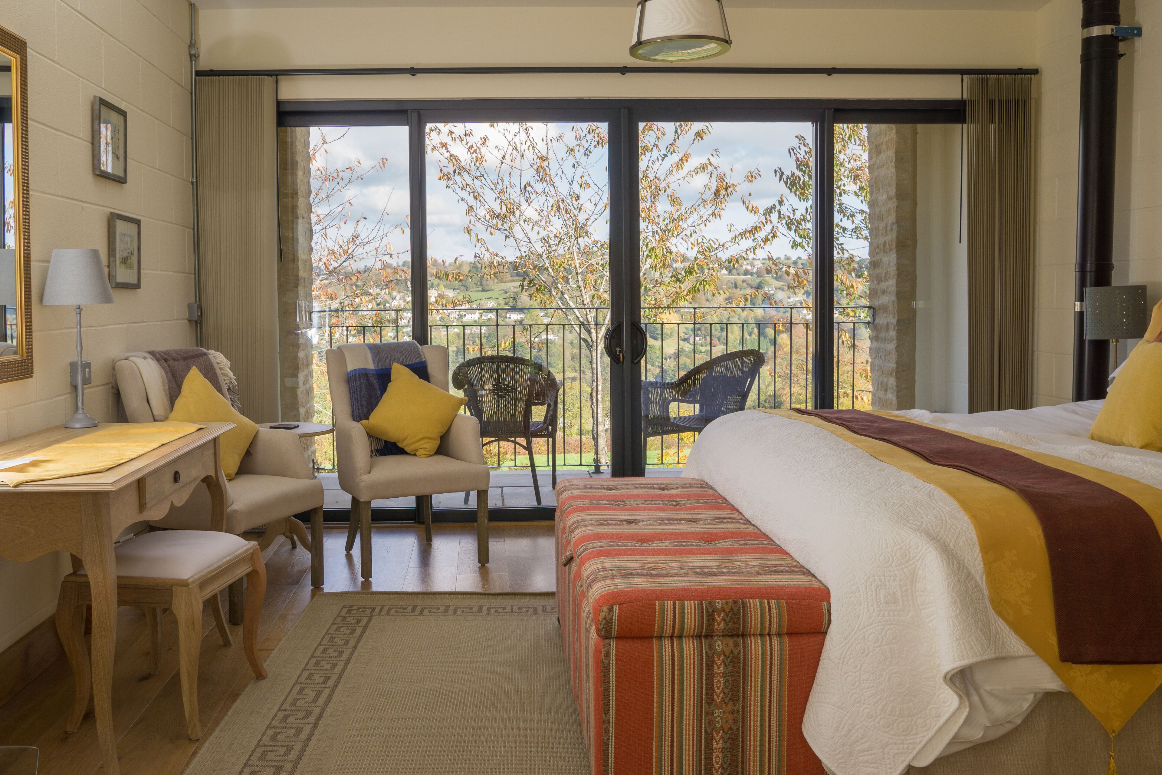 Habitación de hotel con una cama grande, un escritorio, una silla y un balcón con vistas a árboles.