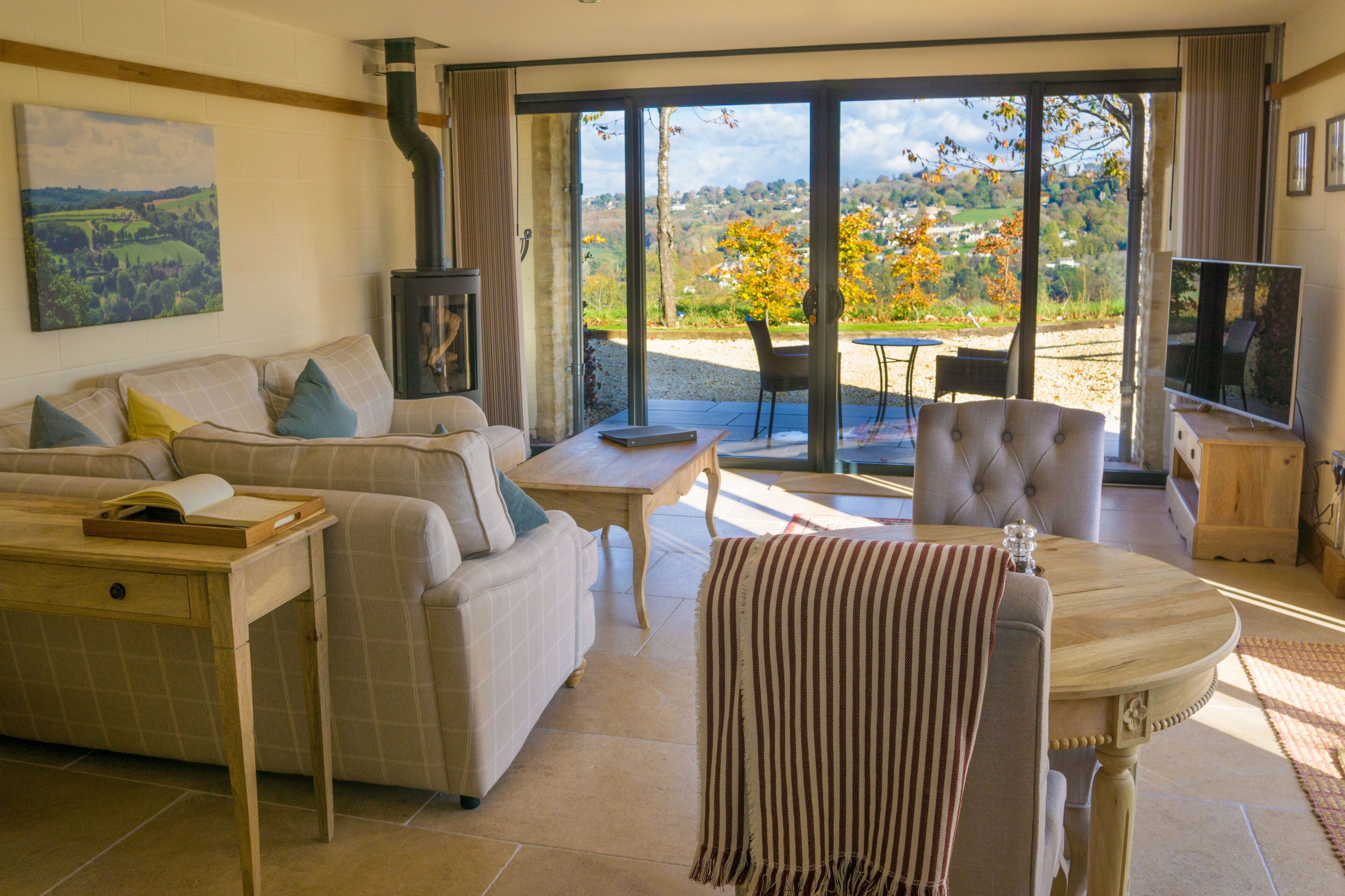 Ein Wohnzimmer mit einer Couch, einem Tisch, einem Fernseher und Blick auf eine Landschaft durch große Glasüren.