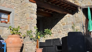 Un edificio de piedra con un balcón de madera, asientos exteriores y plantas en macetas.