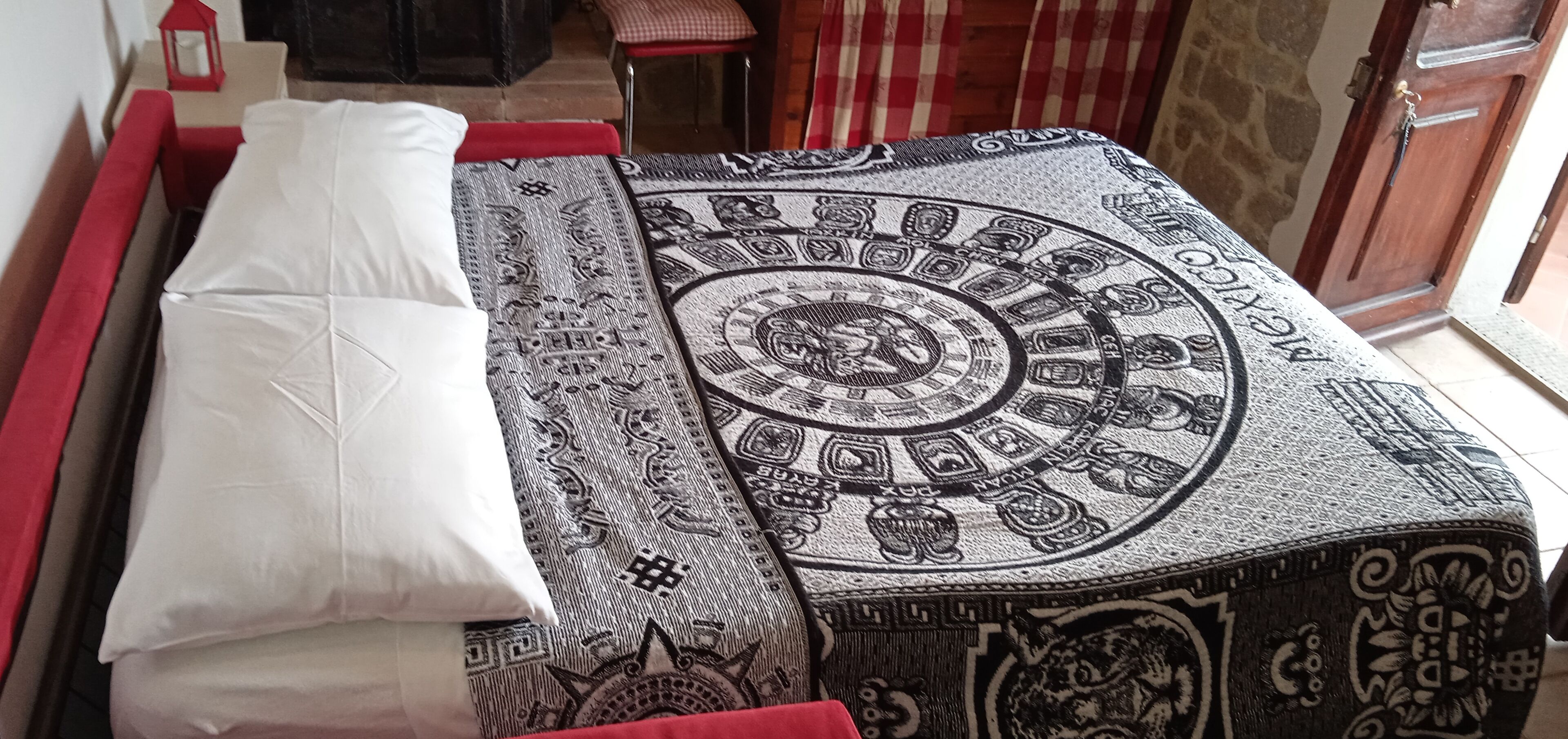A bed with a patterned bedspread and pillows, a red bench, and a door in the background.