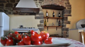 Una cocina con paredes de piedra, estufa a gas y una repisa de madera con botellas de vino.