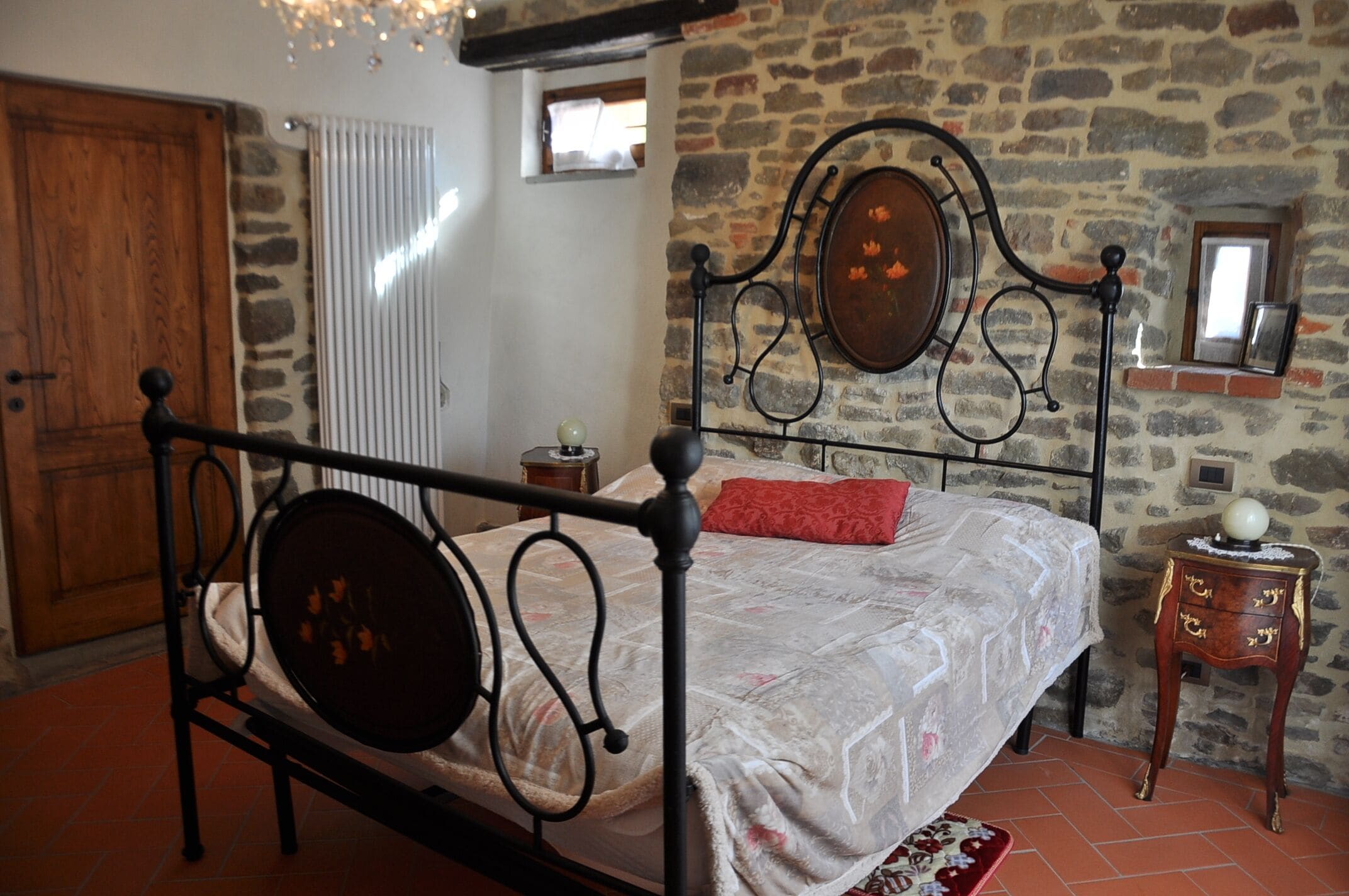 Un letto con struttura in metallo e testiera in legno, un comodino con una lampada e una parete in pietra con una finestra.