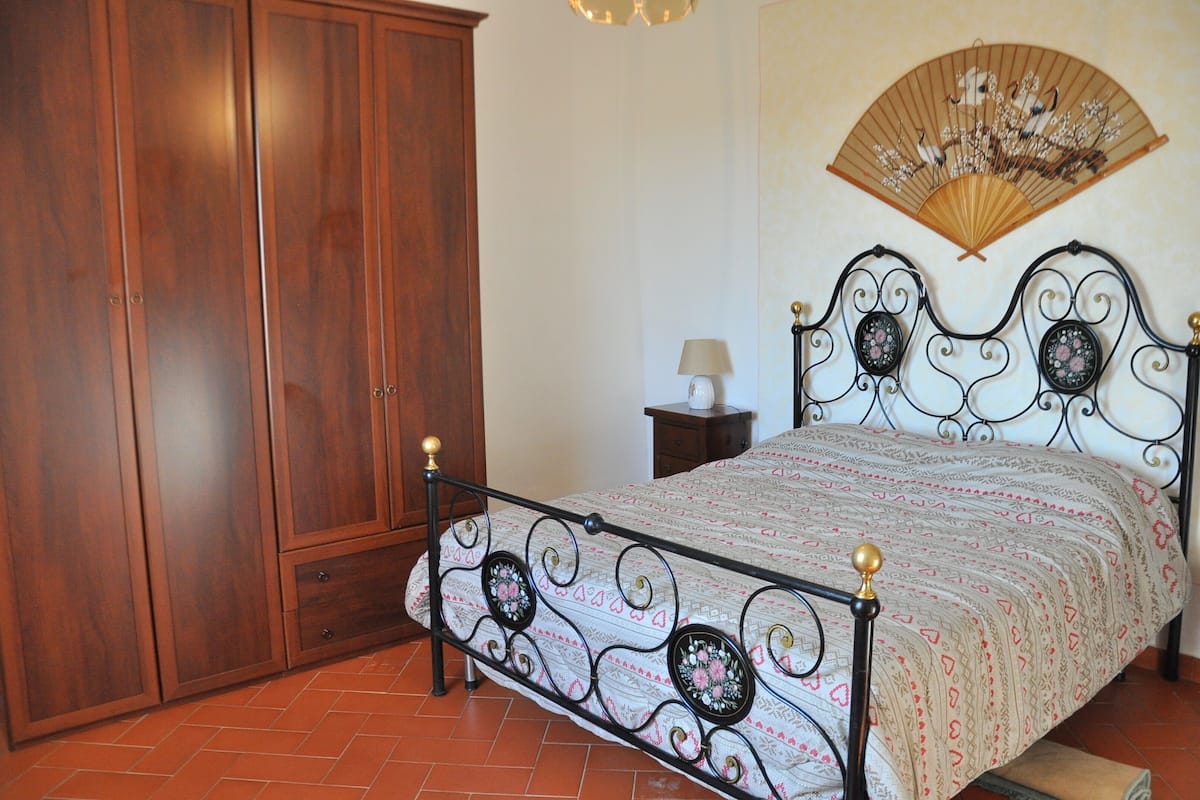 Un dormitorio con cama, armario de madera y un abanico decorativo en la pared.
