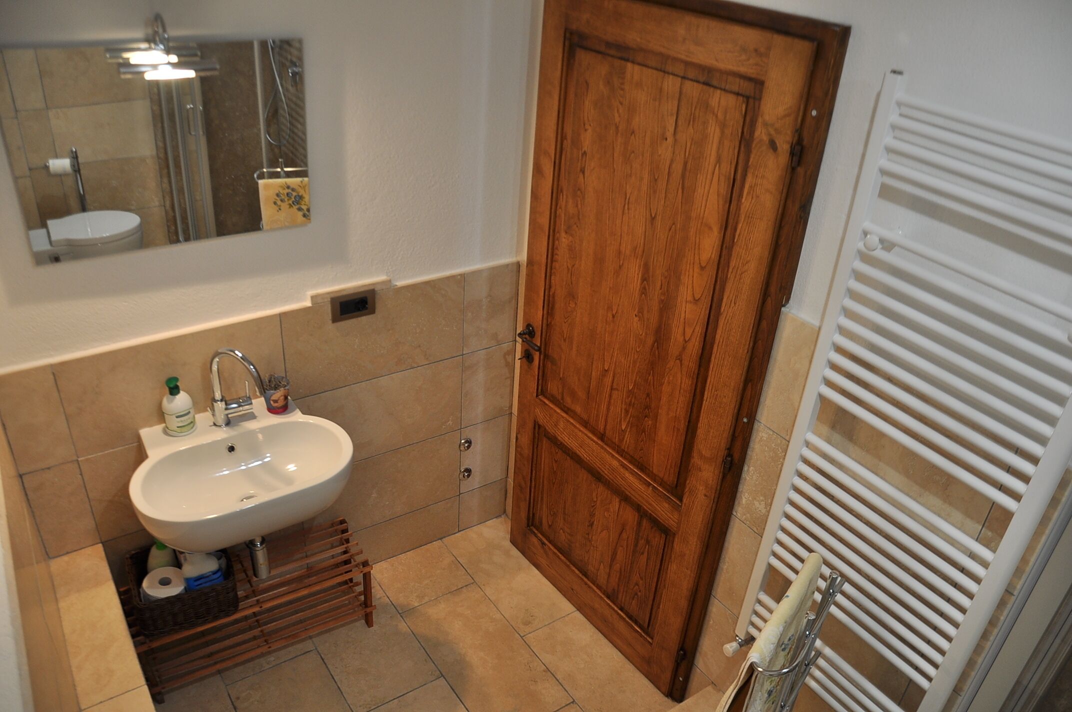 A bathroom with a wooden door, a white sink, and a mirror above it.
