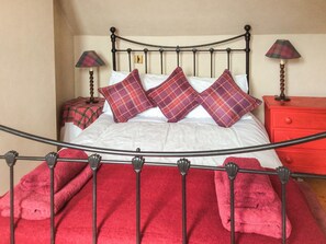 Una cama con estructura metálica, almohadas rojas y una mesita de noche roja.