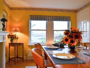 A dining room with a wooden table set for two, a window with a view, and a vase with sunflowers.