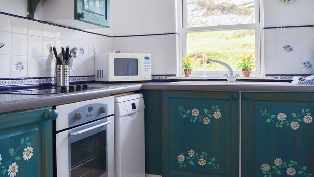 A kitchen with teal cabinets, a white microwave, and a window with a view of greenery. - 2 bedroom accommodation in Fearnbeg, near Applecross (Fearnbeg, near Applecross)