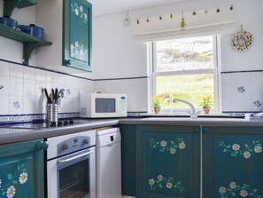 A kitchen with teal cabinets, a white microwave, and a window with a view of greenery. - 2 bedroom accommodation in Fearnbeg, near Applecross (Fearnbeg, near Applecross)