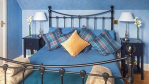 A bed with a metal frame, blue bedding, and plaid pillows. There are two bedside tables with lamps and vases of flowers. - 2 bedroom accommodation in Fearnbeg, near Applecross (Fearnbeg, near Applecross)