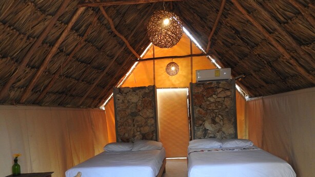 Una habitación acogedora en el ático con dos camas de madera, una pared de piedra, una lámpara colgante y una pequeña mesa con una botella.