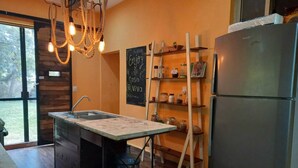 Una cocina moderna con una isla central, un lavamanos integrado, un refrigerador y estantes de madera con frascos.