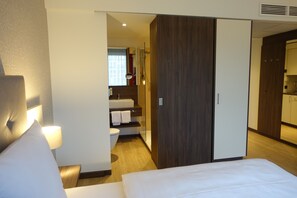A hotel room with a bed, a nightstand, a lamp, a bathroom with a sink and toilet, and a wardrobe. - Heidelberg Hospitality Boarding House (Heidelberg)
