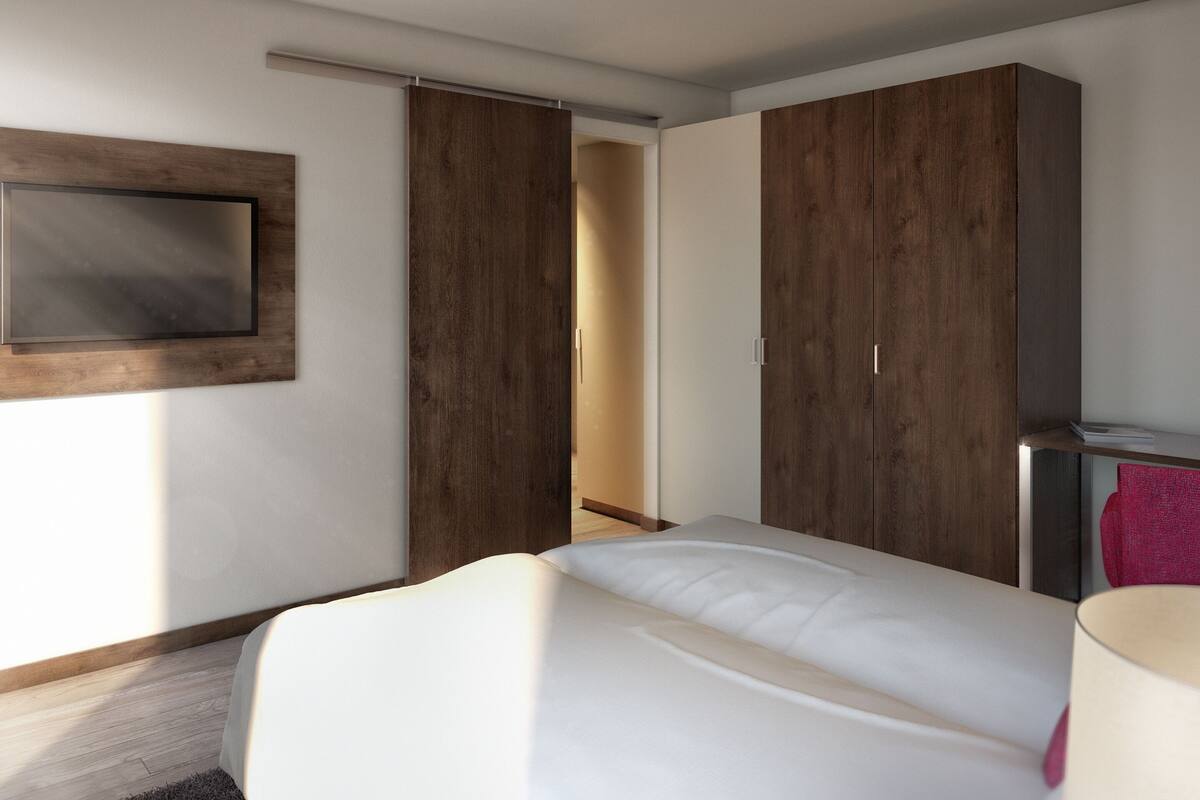 Ein modernes Hotelzimmer mit Bett, Wandfernseher und Kleiderschrank mit Schiebetüren.