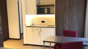 A compact kitchen with a microwave, cabinets, and a dining area with a table and chairs. - Heidelberg Hospitality Boarding House (Heidelberg)
